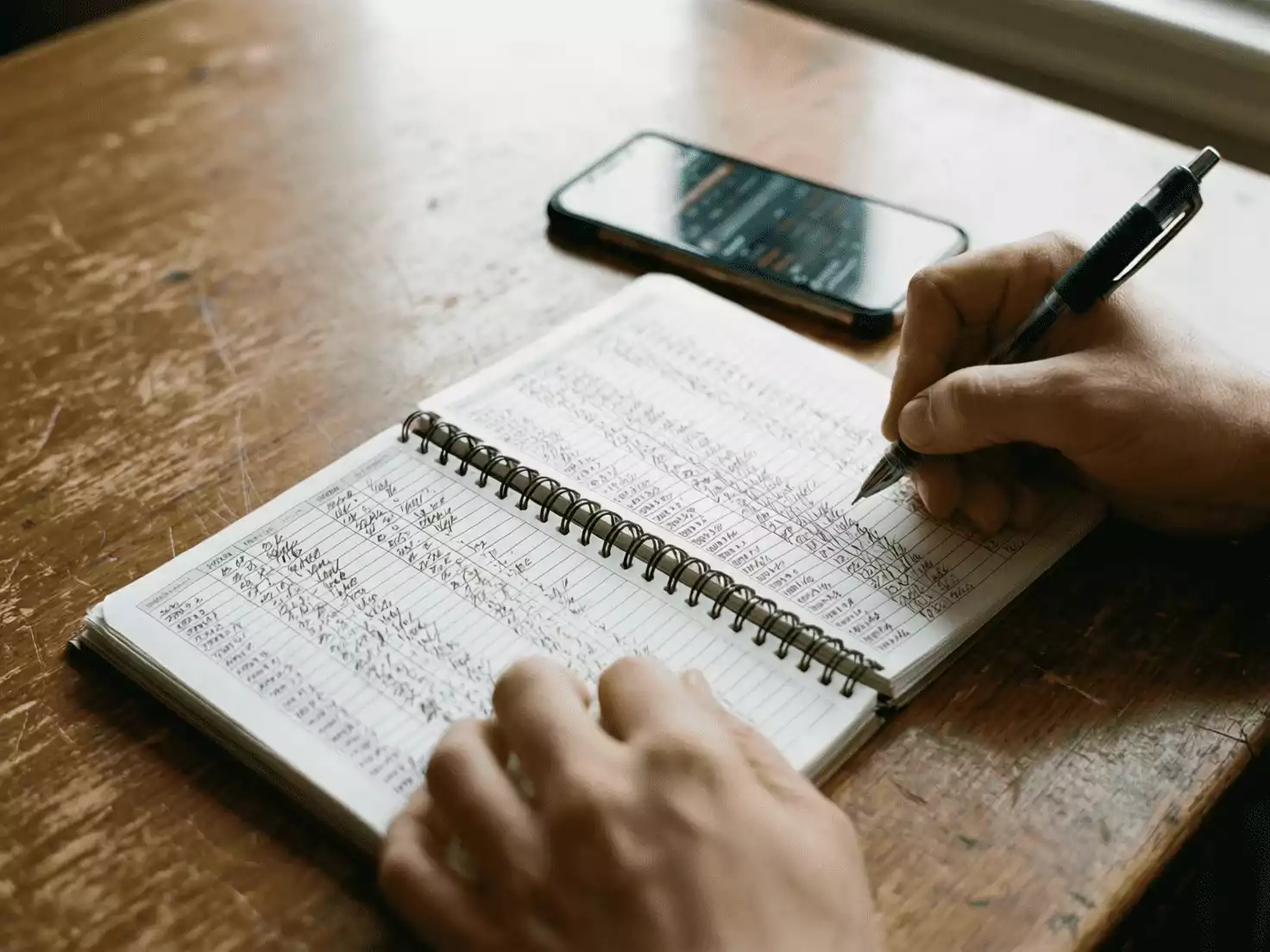 Persona escribiendo en un cuaderno de notas con datos de apuestas